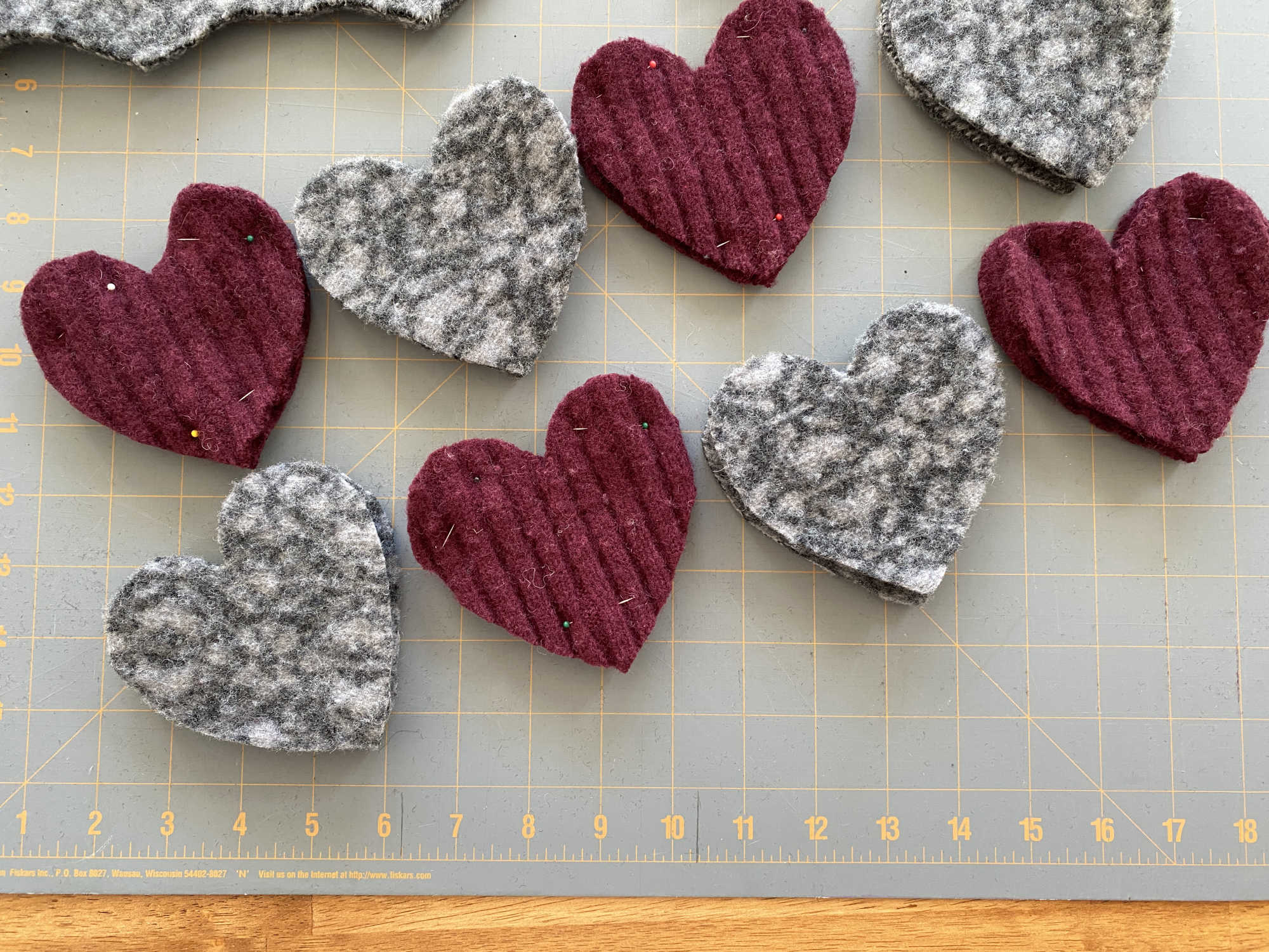 Two rows of alternating maroon and grey felted hearts, pinned and prepped for sewing.
